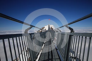 Perspctive view on Steel hanging bridge between ice mountain peak middle blue clear sky background and white cloudy on winter