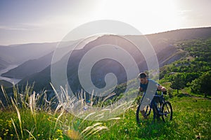 Perspective of a fit mountain biker pushing his bike uphill with amazing view on a forest, river and mountains in the background.
