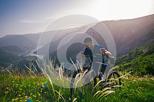 Perspective of a fit mountain biker pushing his bike uphill with amazing view on a forest, river and mountains in the background.