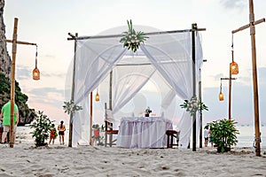 Perspective from the ground, white toned. Tourists enjoy the sunset view on the beach. On the sand set table decorated for a