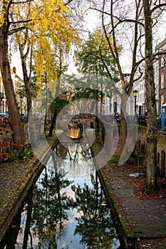 Perspective outdoor view of water reflections of old narrow canal with autumn trees in Amsterdam.