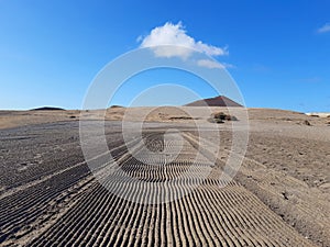 Perspective of sand rutted road in desert and volcanic landscape. Background of raked white sand. Clean beach sand texture with