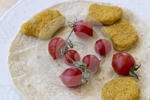 Perspective shot of chicken nuggets and small red fresh tomatoes on the wide white plate as a breakfast with thin bread