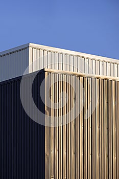 Perspective side view of gray and white corrugated metal wall of industrial buildings against blue sky