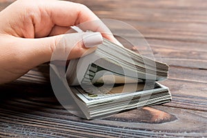 Perspective view of a businesswoman`s hands counting one hundred dollar banknotes on wooden background. Success and wealth concep