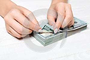Perspective view of a businesswoman`s hands counting one hundred dollar banknotes on wooden background. Success and wealth concep