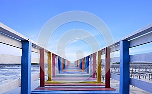 Perspective view of colorful rainbow wooden bridge extends into the sea against blue sky background