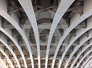 Perspective view of curved arch shaped steel girders under an old road bridge with rivets and struts painted grey