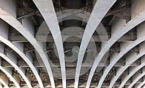 Perspective view of curved arch shaped steel girders under an old road bridge with rivets and struts painted grey