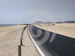 Perspective view of curved asphalt road between sand dunes, volcanic and desert landscape and calm ocean. Lonely road in Idyllic