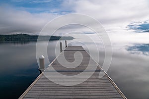 Perspective view of dock over calm lake with blue sky, clouds, and fog