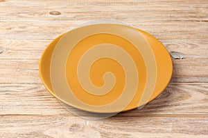 Perspective view. Empty yellow matte plate on orange wooden background