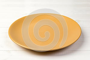 Perspective view. Empty yellow matte plate on white wooden background