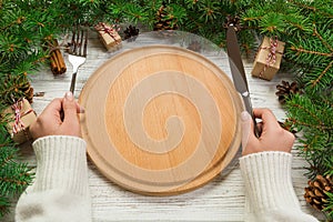 Perspective view girl holds fork and knife in hand and is ready to eat. Empty wood round plate on wooden christmas background. hol