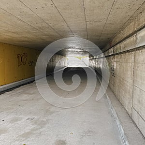Urban pedestrian and bicycle underpass with concrete ceiling and yellow wall, perspective view toward bright daylight exit