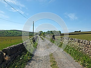 Perspective view of a a long narrow country road surrounded by stone walls and flowers in west yorkshire countryside surrounded