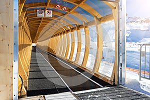 Perspective view of magic carpet transportation ski lift conveyor belt covered with wooden arch roof tunnel at alpine mountain