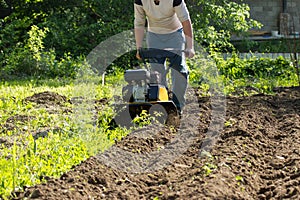 Perspective view of man plowing garden soil by motor cultivator