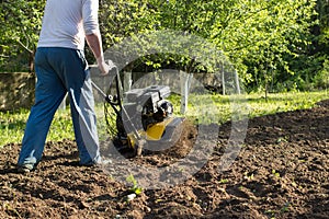 A perspective view of a man during soil plow process by motor cultivator