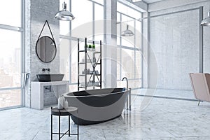 Perspective view on modern black bath in huge sunlit loft style bathroom with metallic furniture, round mirror on concrete wall