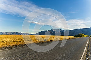 Perspective view of road trip on asphalt road with beautiful nature golden yellow grass and mountains in autumn in cloudy blue sky