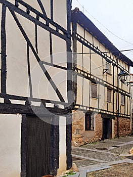 Perspective view of rough white cement wall facades with black wooden slats and old small windows. Detail of beams, lumber and