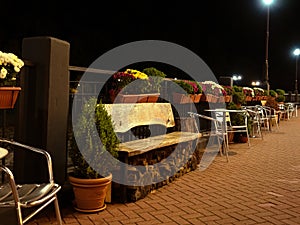 A perspective view of the sidewalk with a metal railing bench and chairs and flower pots along them