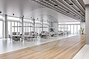 Perspective view on stylish sunlit coworking office with wooden and concrete floor, grey furniture with modern computers, lattice