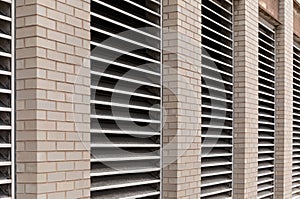 Perspective view of wall of an urban commercial building with numerous inset HVAC air exhaust vents, light colored brick