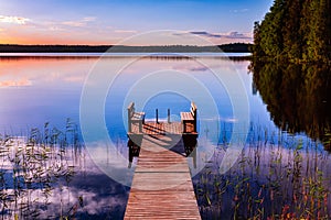 Perspective view of a wooden pier with chairs on the lake at sunset