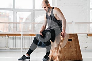 Perspiring fit sportsman resting with towel after hard cross workout in sport hall