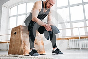 Perspiring fit sportsman resting with towel after hard crossfit workout in light hall