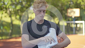 Perspiring sportsman wiping face with white towel and sighing. Portrait of young redhead Caucasian man standing on