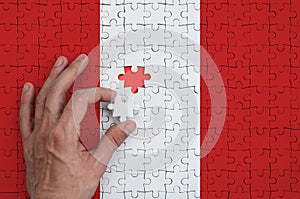 Peru flag is depicted on a puzzle, which the man`s hand completes to fold