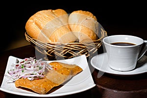 Peruvian breakfast, popular Peruvian tamale with onion sauce, breads and a cup of coffee on a table.