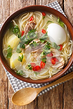 Peruvian caldo de gallina chicken noodle soup close-up in a plate. vertical top view photo