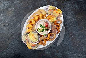 PERUVIAN FOOD. Piqueo caliente. Hot seafood platter fried shrimps, squid rings and baked scallops with sauce