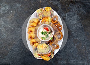 PERUVIAN FOOD. Piqueo caliente. Hot seafood platter fried shrimps, squid rings and baked scallops with sauce