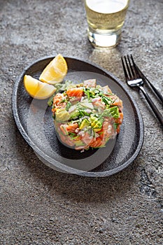 PERUVIAN NIKKEI FOOD. Salmon avocado ceviche on black plate, black background top view