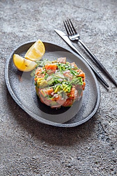 PERUVIAN NIKKEI FOOD. Salmon avocado ceviche on black plate, black background top view