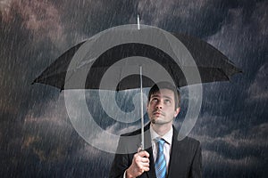 Pessimistic businessman with black umbrella in storm.