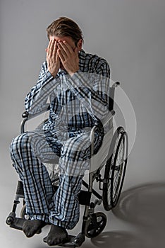 Pessimistic cripple in chair covering his face with hands
