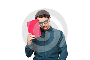 Pessimistic student guy looking down upset, as holds a book isolated on white background. Confused young man has learning troubles