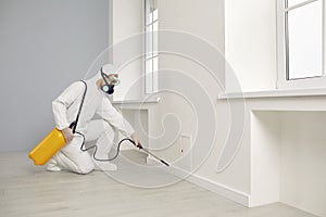 Pest control service worker in protective uniform spraying insecticide inside the house