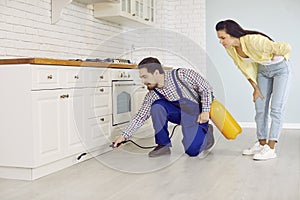 Pest control service worker spraying cockroach insecticide under kitchen cabinets