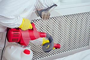 Pest control worker lying on floor and spraying pesticides in bedroom