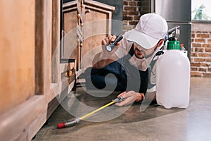 pest control worker lying on floor and spraying pesticides under cabinet