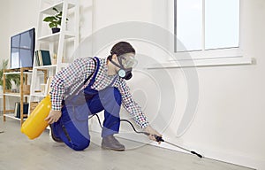 Pest control worker in a mask and overalls spraying insecticide inside the house