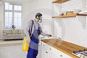 Pest control worker in mask spraying termite or cockroach insecticide in the kitchen