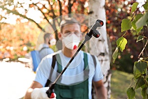 Pest control worker outdoors, focus on insecticide sprayer